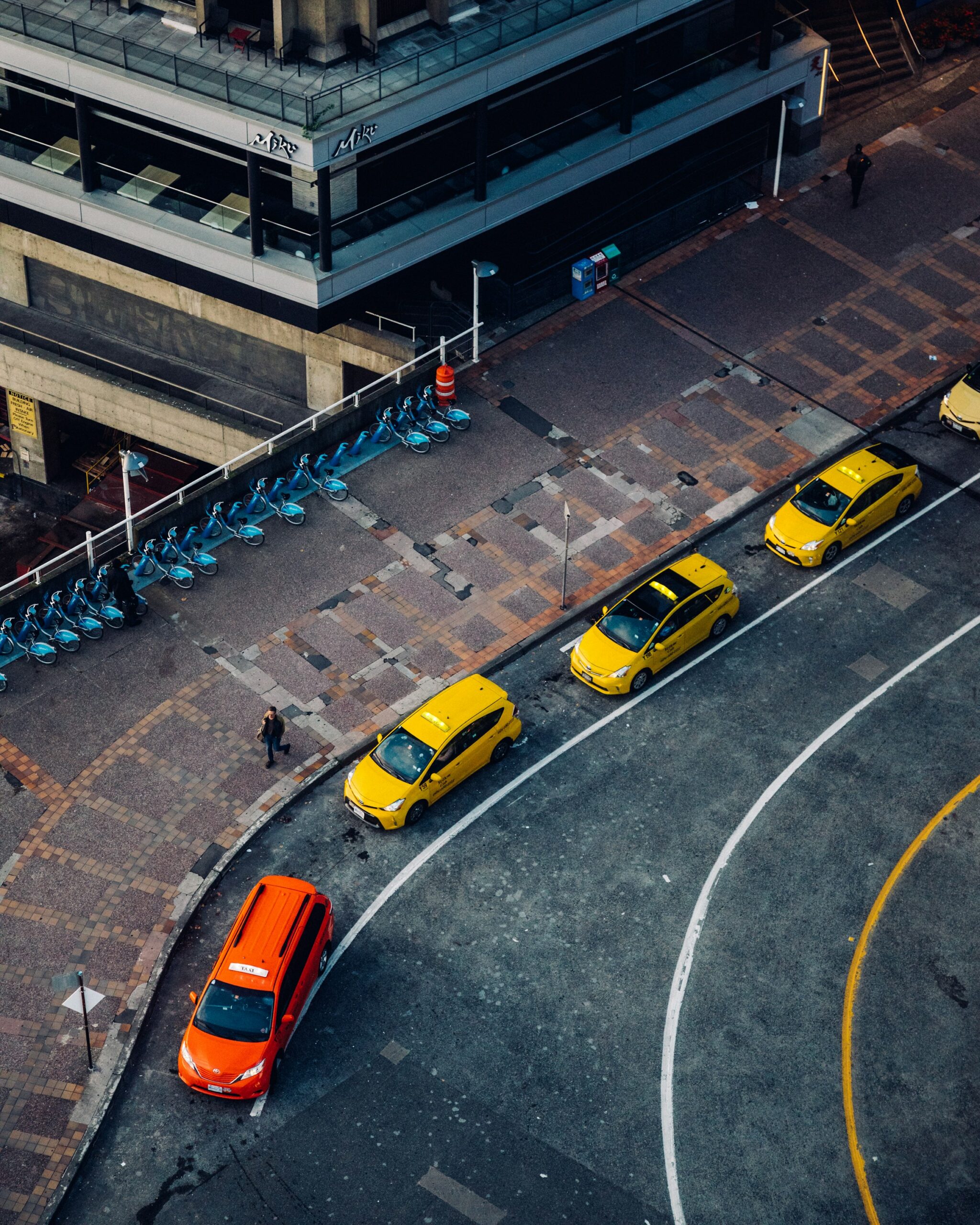 Overhead photo of one accessible taxi and 4 non-accessible taxis queuing in front of Miku restaurant in Vancouver near Canada Place by Wes Hicks on Unsplash.