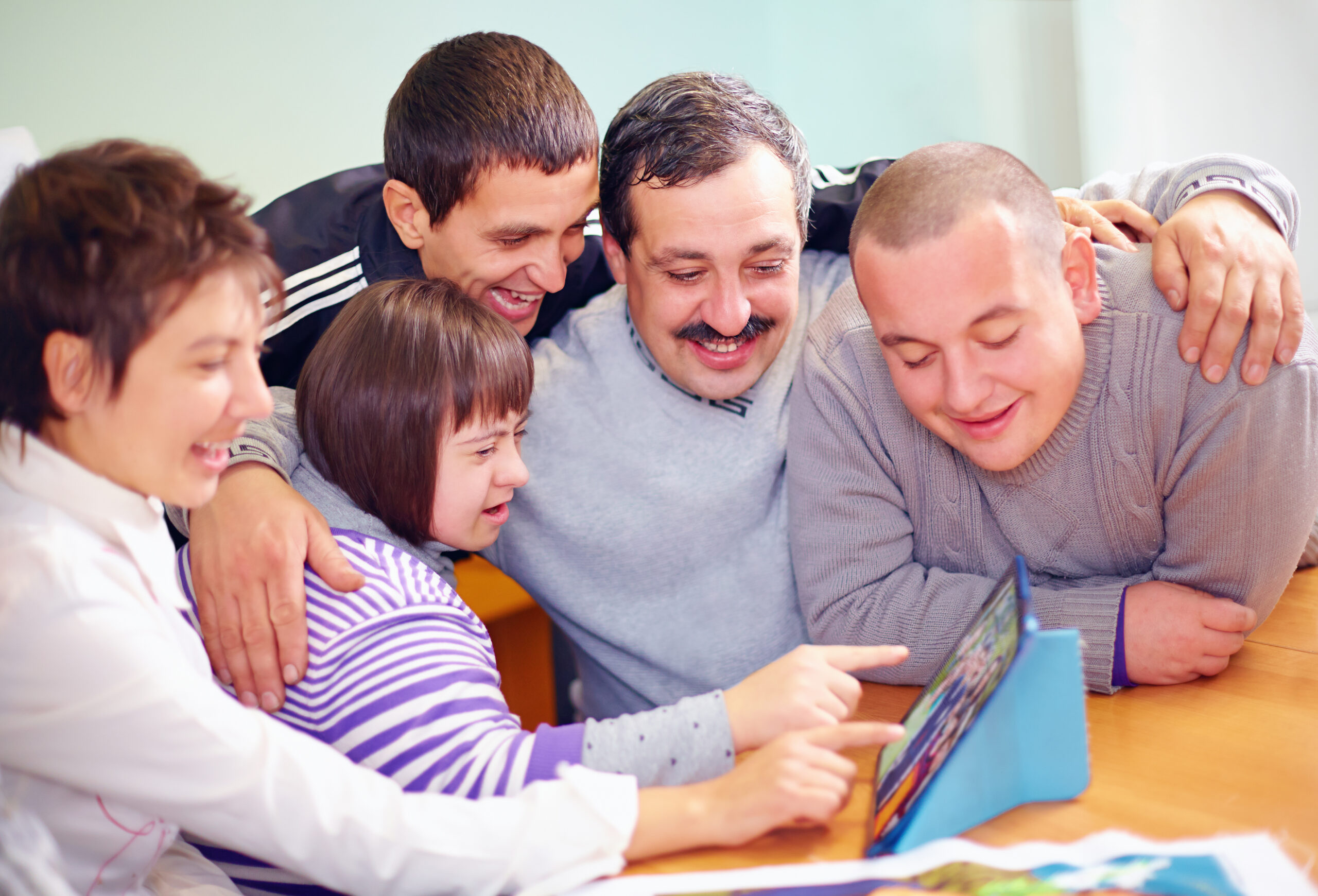 A family of 2 parents and 3 kids, many visibly and proudly disabled, gather around a tablet.